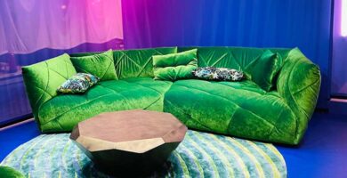 Knallgrünes Sofa mit achteckigen Couchtisch auf bluem Teppich mit roter und blauer Beleuchtung.