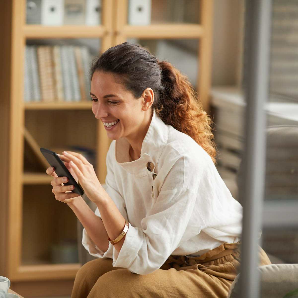 Junge Frau schaut glücklich auf ihr Smartphone.
