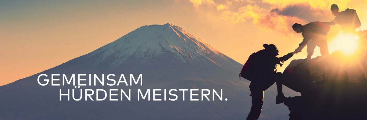 Bild von drei Bergsteigern, die sichgegenseitig nach oben untersützen. Im Hintergrund ist ein Sonnenuntergang zu sehen. Darauf steht "Gemeinsam Hürden meistern". – Ein Symbolbild für der Alliance-Verband Antworten auf die Herausforderungen im Möbelhandel findet.