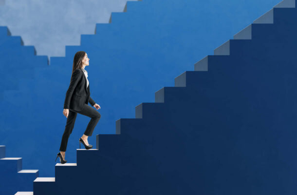 Aufbruch statt Rückblick – Geschäftsfrau steigt selbstbewusst eine blaue Treppe hinauf und symbolisiert berufliche Entwicklung, Fortschritt und neue Perspektiven.