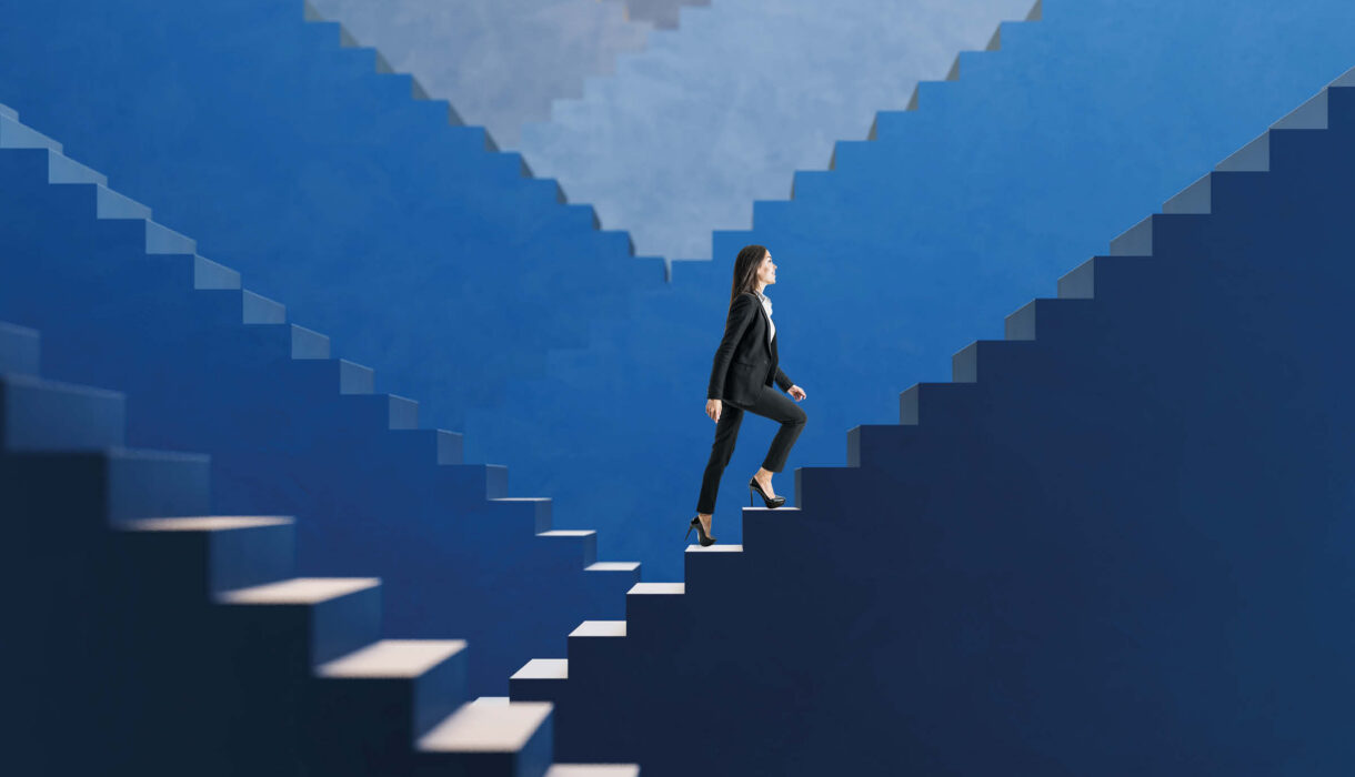 Aufbruch statt Rückblick – Geschäftsfrau steigt selbstbewusst eine blaue Treppe hinauf und symbolisiert berufliche Entwicklung, Fortschritt und neue Perspektiven.