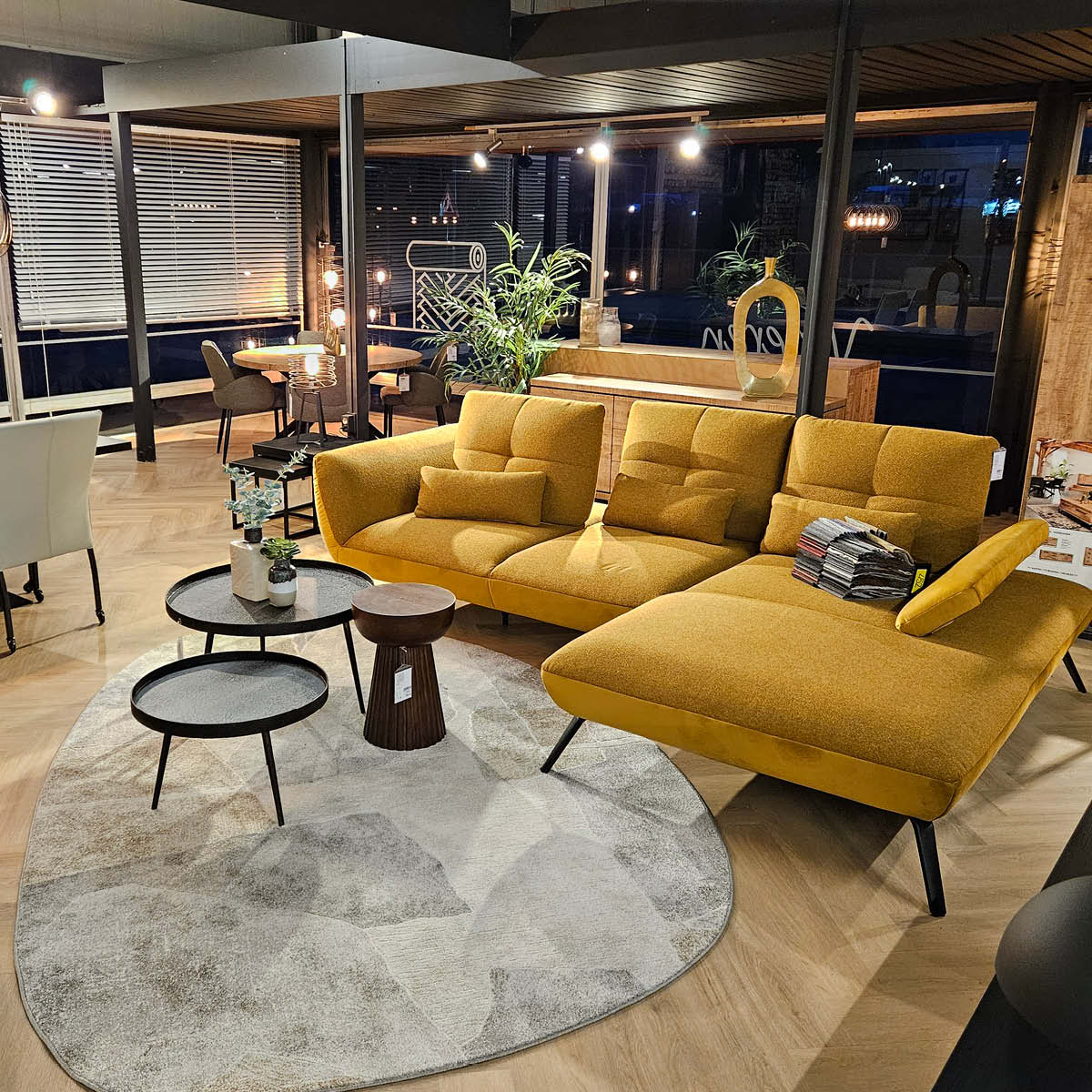 Stilvolle Wohnzimmerausstellung mit gelbem Sofa, Couchtischen und dekorativer Beleuchtung in modernem Möbelhaus-Showroom