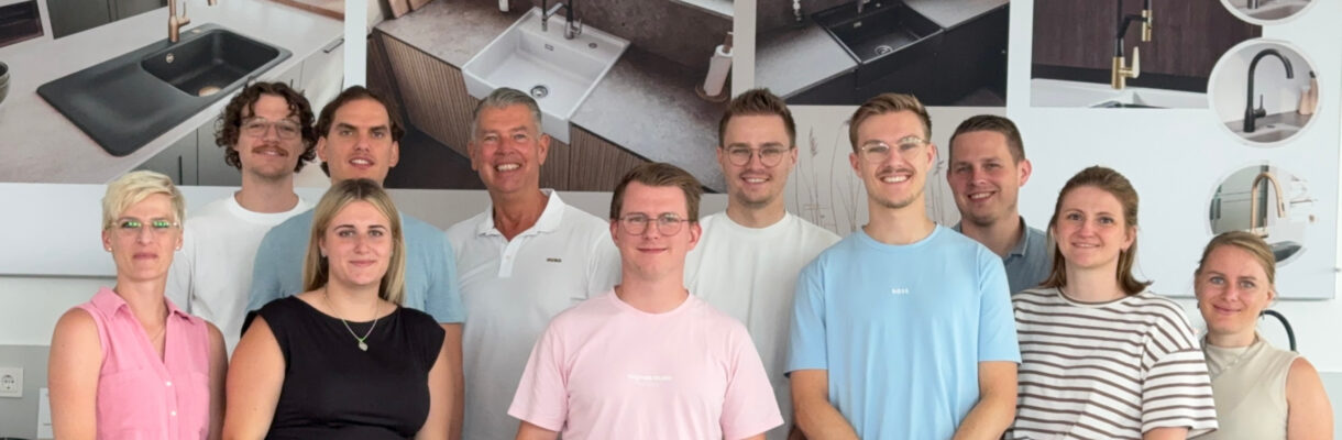 Teamfoto einer Besuchergruppe im Küchenstudio vor Ausstellungswänden mit Spülen und Armaturen als Inspiration für Küchenplanung, Küchenmöbel und moderne Designküchen.