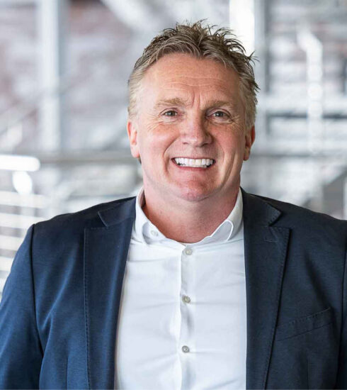 Professionelles Porträt eines lächelnden Mannes im dunklen Sakko vor modernem Innenraum – Ansprechpartner im Möbel- und Küchenverband für Küchenstudios, Küchenplanung und Möbelhandel.