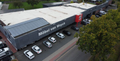 Luftaufnahme des Möbelhauses Möbel van Weyck mit großer grauer Fassade, Kundenparkplätzen und weitläufigem Flachdach – Standort für Möbel, Küchenstudio, individuelle Küchenplanung und Einrichtung.