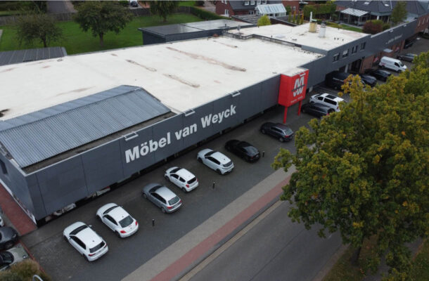 Luftaufnahme des Möbelhauses Möbel van Weyck mit großer grauer Fassade, Kundenparkplätzen und weitläufigem Flachdach – Standort für Möbel, Küchenstudio, individuelle Küchenplanung und Einrichtung.