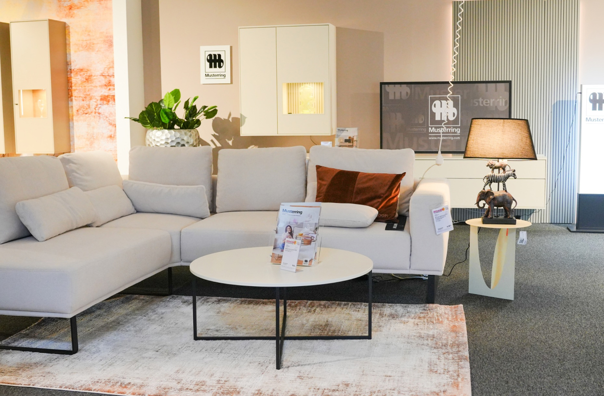Wohnbereich mit hellem Ecksofa, runden Couchtischen und Stehleuchte in der Möbelausstellung.