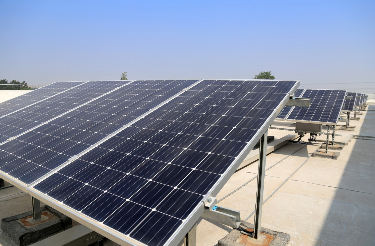 Photovoltaikanlage mit mehreren Reihen Solarmodulen auf einem Flachdach bei blauem Himmel.