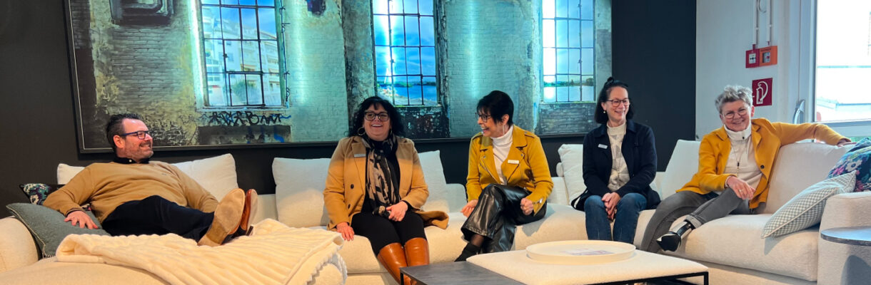 Fünf Personen sitzen auf einer hellen Sofalandschaft in der Möbelausstellung – Möbel May im Porträt.