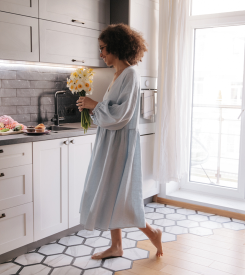 Frau mit Blumen in einer hellen modernen Küche mit weißen Fronten, dunkler Arbeitsplatte und großen Fensterflächen – wohnliche Küchenatmosphäre bei Alliance Küchen.