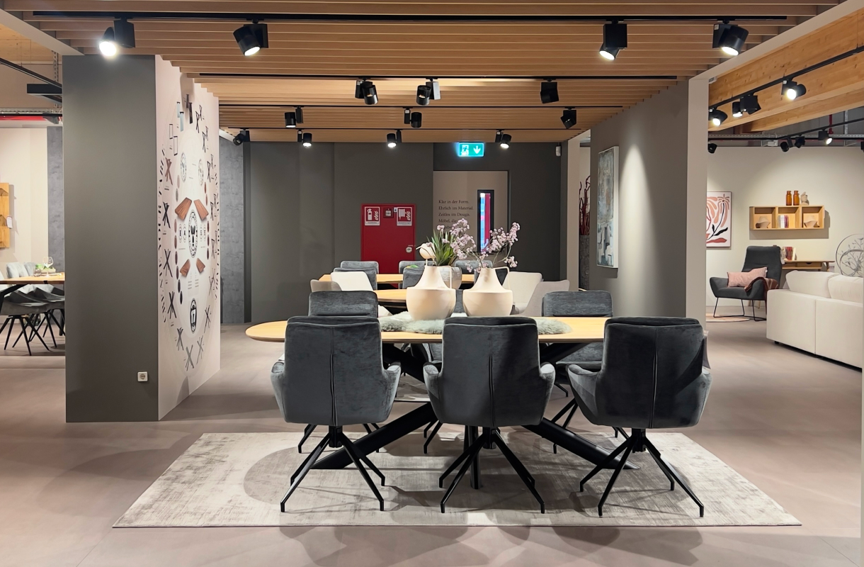 Möbelausstellung mit einem Holzesstisch, dunkelgrauen Polsterstühlen und dekorativen Vasen.