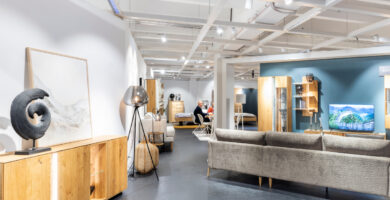 Möbelausstellung mit grauem Sofa, Sessel und Holzmöbeln auf einer großzügigen Ausstellungsfläche.