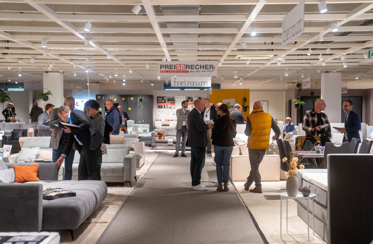Besucher im Gespräch in einer Möbelausstellung mit Sofas und Sesseln.